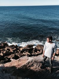 Man standing on rock by sea against sky