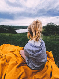 Rear view of girl sitting on yellow blanket against sky