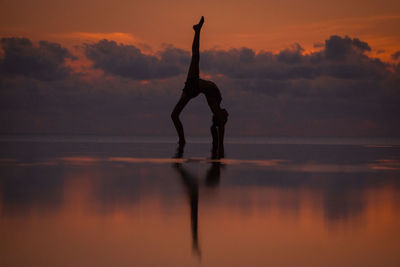 Silhouette man with arms raised against sky during sunset