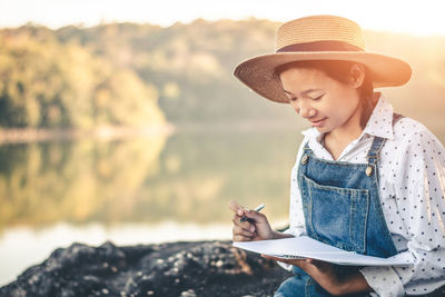 Young woman wearing hat while standing by lake