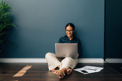 Young woman using laptop while sitting on floor at home