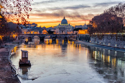 Arch bridge over river with st peter church in background during sunset