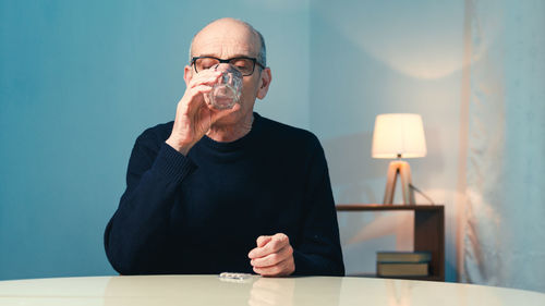 Elderly man with eyeglasses sitting at the table at home eats a heart pill