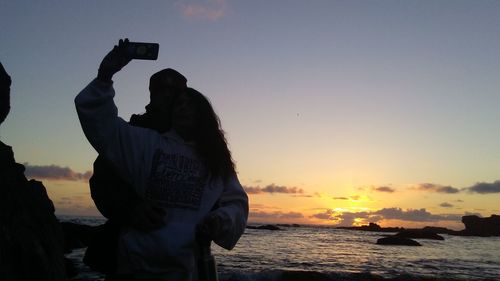 Silhouette man photographing at beach during sunset