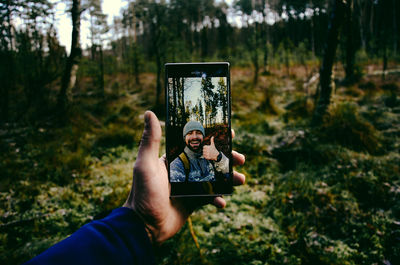Cropped hand of man taking selfie in forest