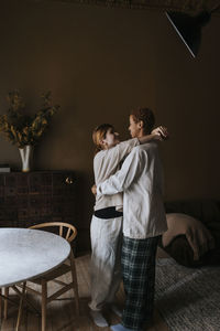 Romantic non-binary couple standing with arms around each other at home