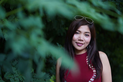 Portrait of smiling young woman standing by plants in park