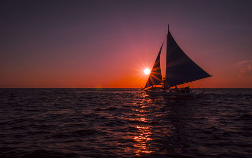 Silhouette sailboat sailing on sea against clear sky during sunset