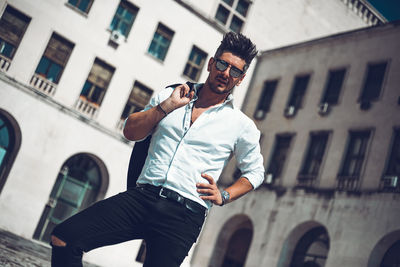 Portrait of man standing against building in city during sunny day