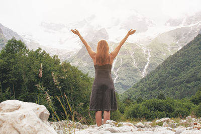 Rear view of woman with arms raised standing on mountain