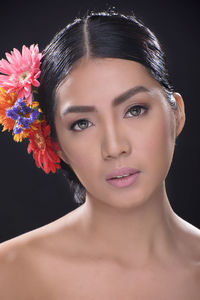 Close-up portrait of beautiful woman wearing flowers against black background