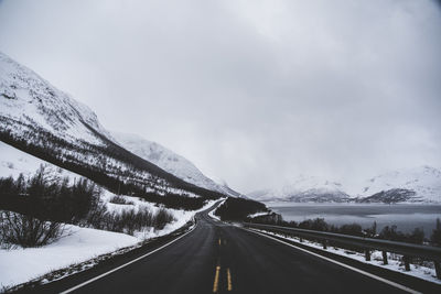Empty road by snowcapped mountain against sky
