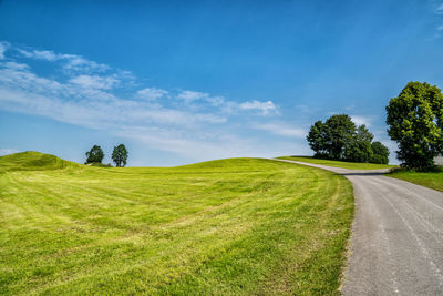 Empty road amidst field against sky