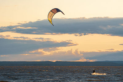 Silhouette person paragliding over sea against sky