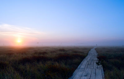 Footpath amidst field against sky during sunset