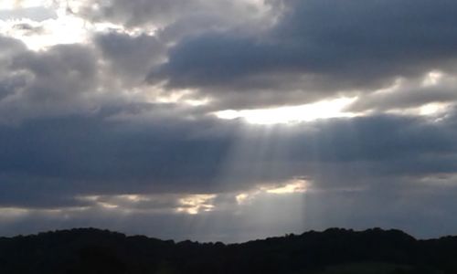 Low angle view of sunlight streaming through clouds