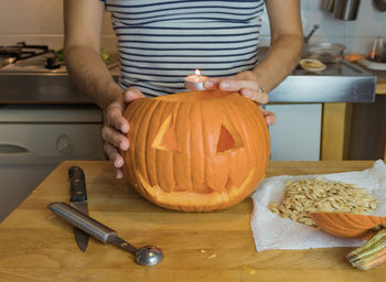 Midsection of man holding pumpkin on table at home