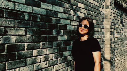 Woman wearing sunglasses while standing against brick wall