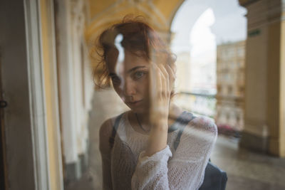 Portrait of young woman looking away while standing against window