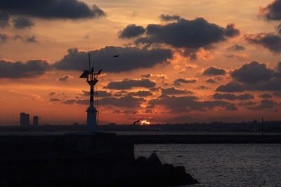 Silhouette tower by sea against sky during sunset