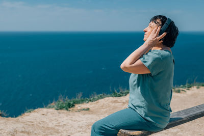 Portrait adult woman listens to music in headphones in summer, spring against the backdrop mountains