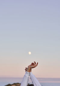 Unrecognizable crop female standing with raised arms on background of sunset sky with moon and enjoying freedom during vacation in summer