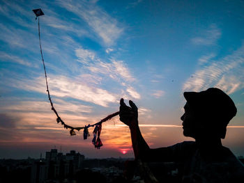 Low angle view of silhouette man holding cityscape against sky during sunset