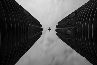 Low angle view of modern buildings against sky with airplane 