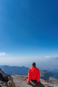 Rear view of man standing on mountain against clear blue sky