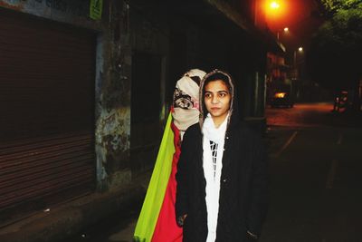 Portrait of happy woman standing against illuminated wall
