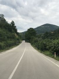 Empty road along trees and mountains against sky