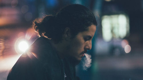 Profile view of man smoking in city at night