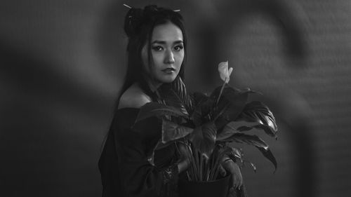 Portrait of young woman standing against plant