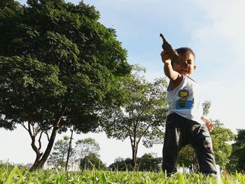 Low angle view of boy standing by tree against sky