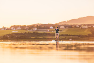 Man standing in lake against sky during sunset