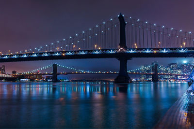 Manhattan bridge over river against sky at night