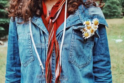 Midsection of woman wearing denim jacket with flowers on field
