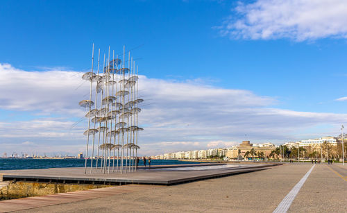 Cranes on road by sea against sky in city