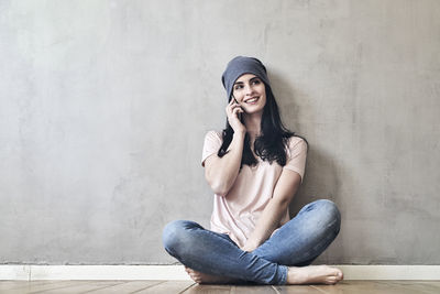 Smiling young woman sitting on the floor talking on cell phone