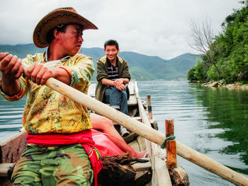 Men sitting by lake against sky