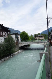 Bridge over river by buildings against sky