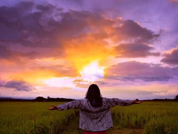 Rear view of woman standing on field against sky during sunset