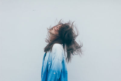 Waist up side view of young woman tossing her hair against white wall