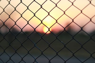 Close-up of chainlink fence against sky during sunset