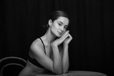 Portrait of young woman sitting against black background