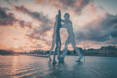 Molecule men over spree river against cloudy sky