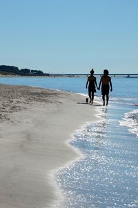 People walking on beach against clear blue sky