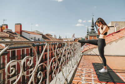 Low angle view of young woman standing on bridge against clear sky