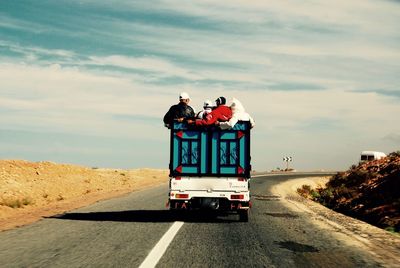 People in vehicle on road at desert against sky