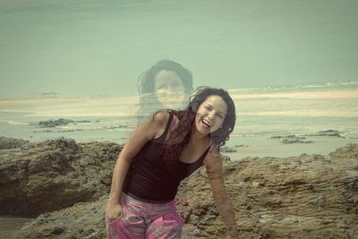 Happy young woman standing on beach against sky